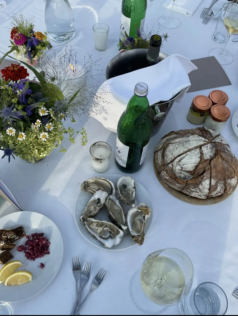 Gedeckte Tafel mit Austern, Brot, Weißwein und Wiesenblumen