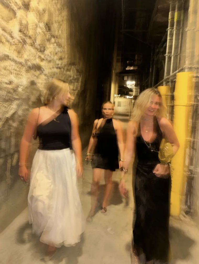 Drei Frauen in Abendkleidern gehen lachend durch eine nächtliche Gasse